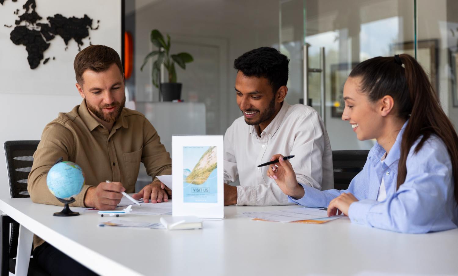 Three professionals discussing job opportunities around a table with a globe and travel brochures in the background, representing Work Abroad Agencies